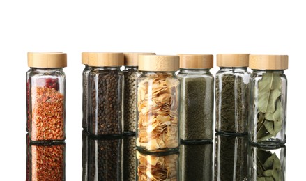 Photo of Many different aromatic spices in jars on mirror surface against white background