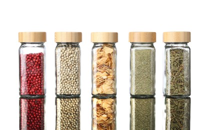 Photo of Many different aromatic spices in jars on mirror surface against white background