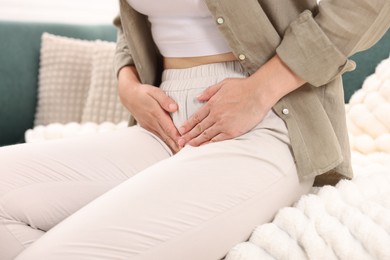Photo of Woman suffering from cystitis symptoms on sofa at home, closeup