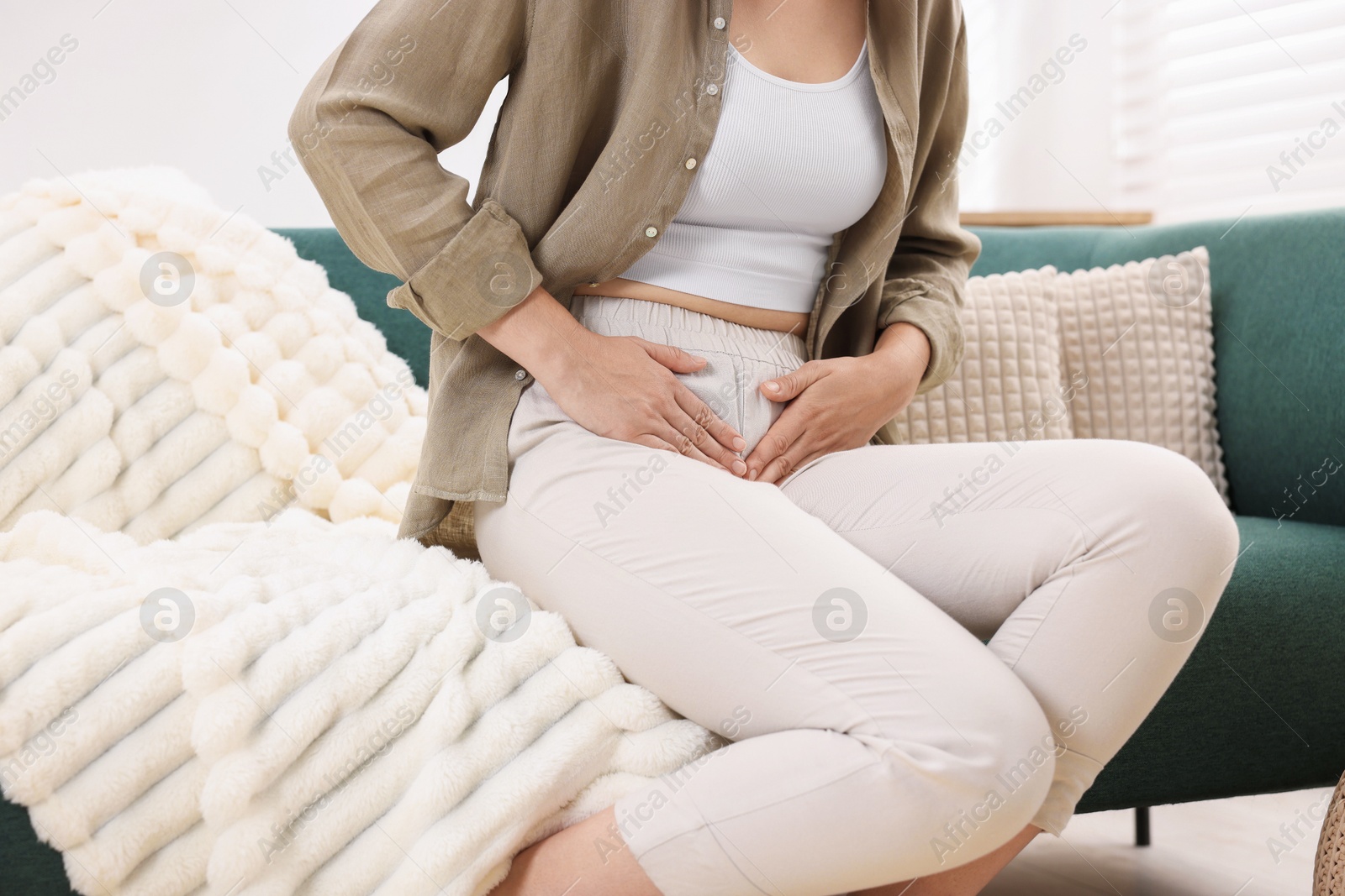 Photo of Woman suffering from cystitis symptoms on sofa at home, closeup