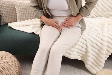 Photo of Woman suffering from cystitis symptoms on sofa at home, closeup