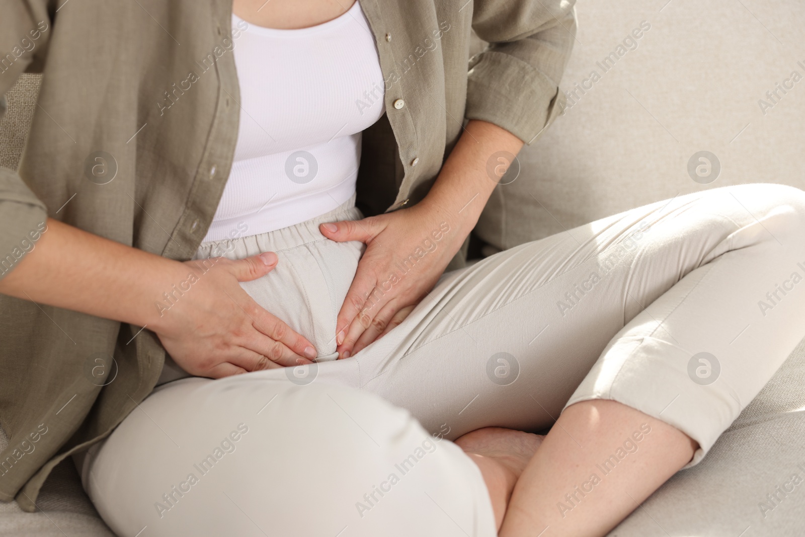 Photo of Woman suffering from cystitis symptoms on sofa at home, closeup