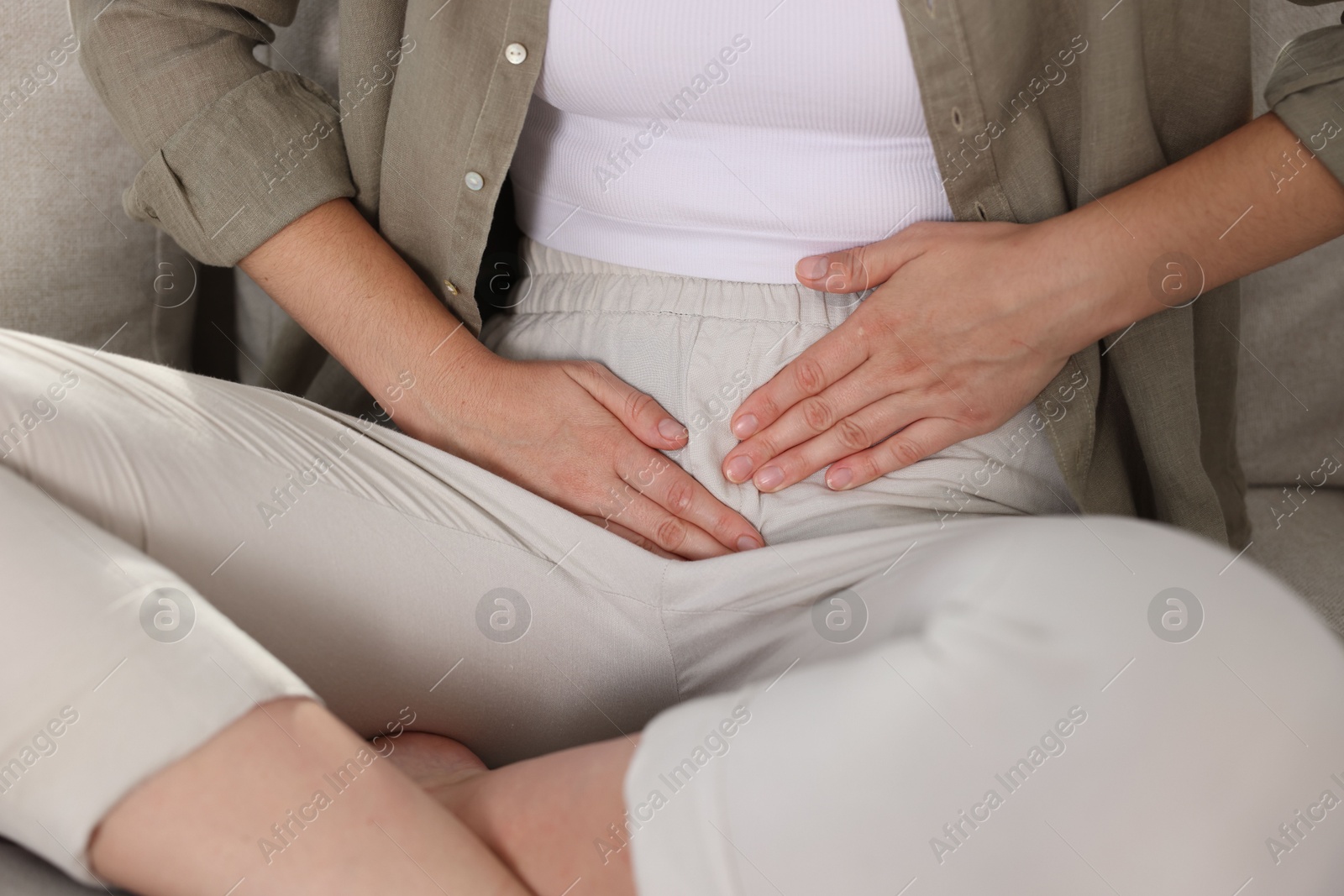 Photo of Woman suffering from cystitis symptoms on sofa at home, closeup