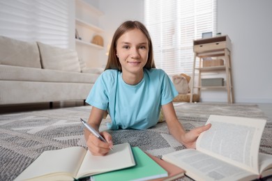 Photo of Teenage girl studying with books on floor at home