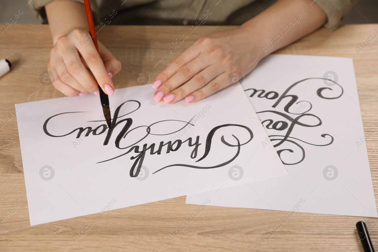 Calligraphy. Woman with brush writing words Thank You on sheet of paper at wooden table, closeup Photo of Calligraphy. Woman with brush writing words Thank You on sheet of paper at wooden table, closeup