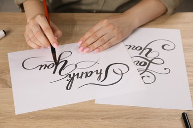 Photo of Calligraphy. Woman with brush writing words Thank You on sheet of paper at wooden table, closeup