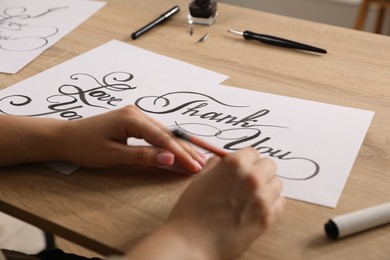 Photo of Calligraphy. Woman with brush writing words Thank You on sheet of paper at wooden table, closeup