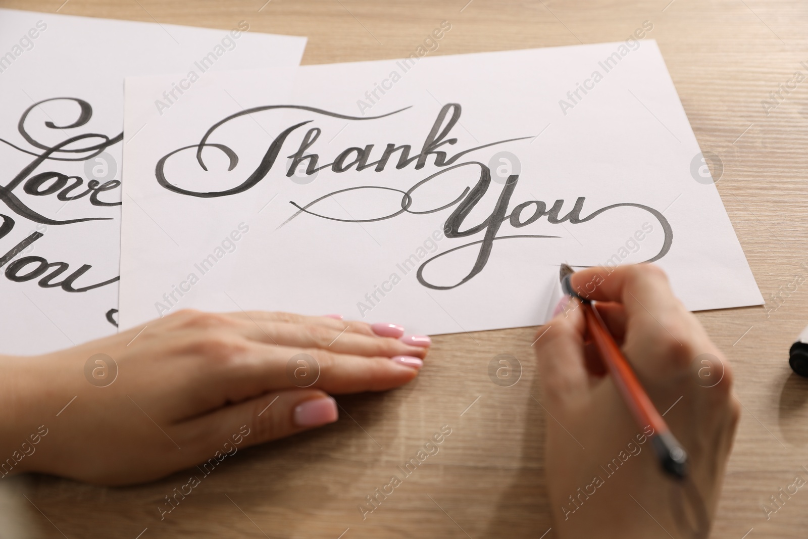 Calligraphy. Woman with brush writing words Thank You on sheet of paper at wooden table, closeup Photo of Calligraphy. Woman with brush writing words Thank You on sheet of paper at wooden table, closeup