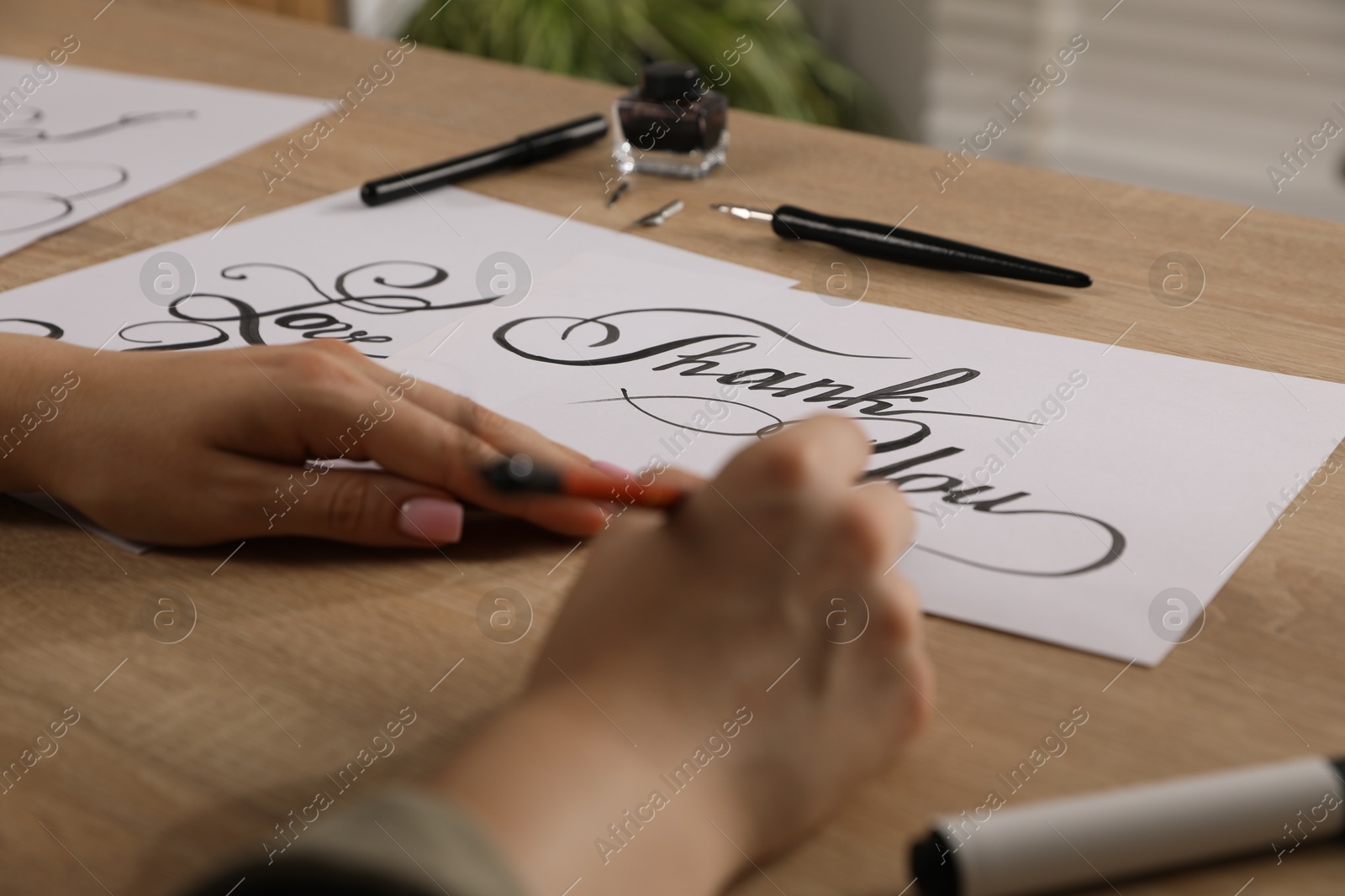 Calligraphy. Woman with brush writing words Thank You on sheet of paper at wooden table, closeup Photo of Calligraphy. Woman with brush writing words Thank You on sheet of paper at wooden table, closeup