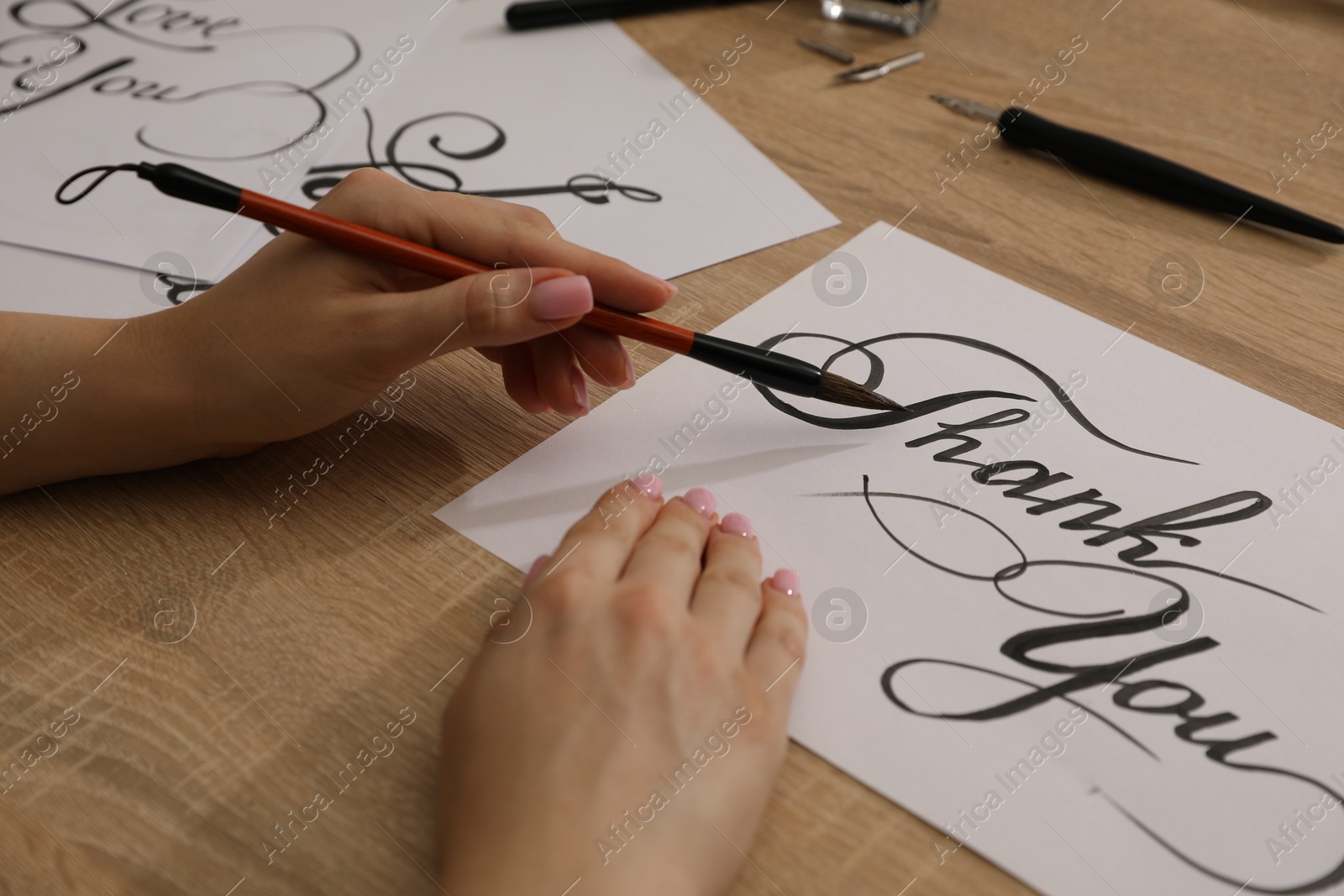 Calligraphy. Woman with brush writing words Thank You on sheet of paper at wooden table, closeup Photo of Calligraphy. Woman with brush writing words Thank You on sheet of paper at wooden table, closeup