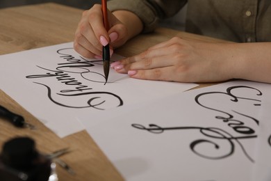 Photo of Calligraphy. Woman with brush writing words Thank You on sheet of paper at wooden table, closeup
