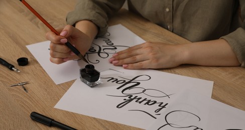Photo of Woman with calligraphy tools and handwritten cards at wooden table, closeup