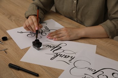 Photo of Woman with calligraphy tools and handwritten cards at wooden table, closeup