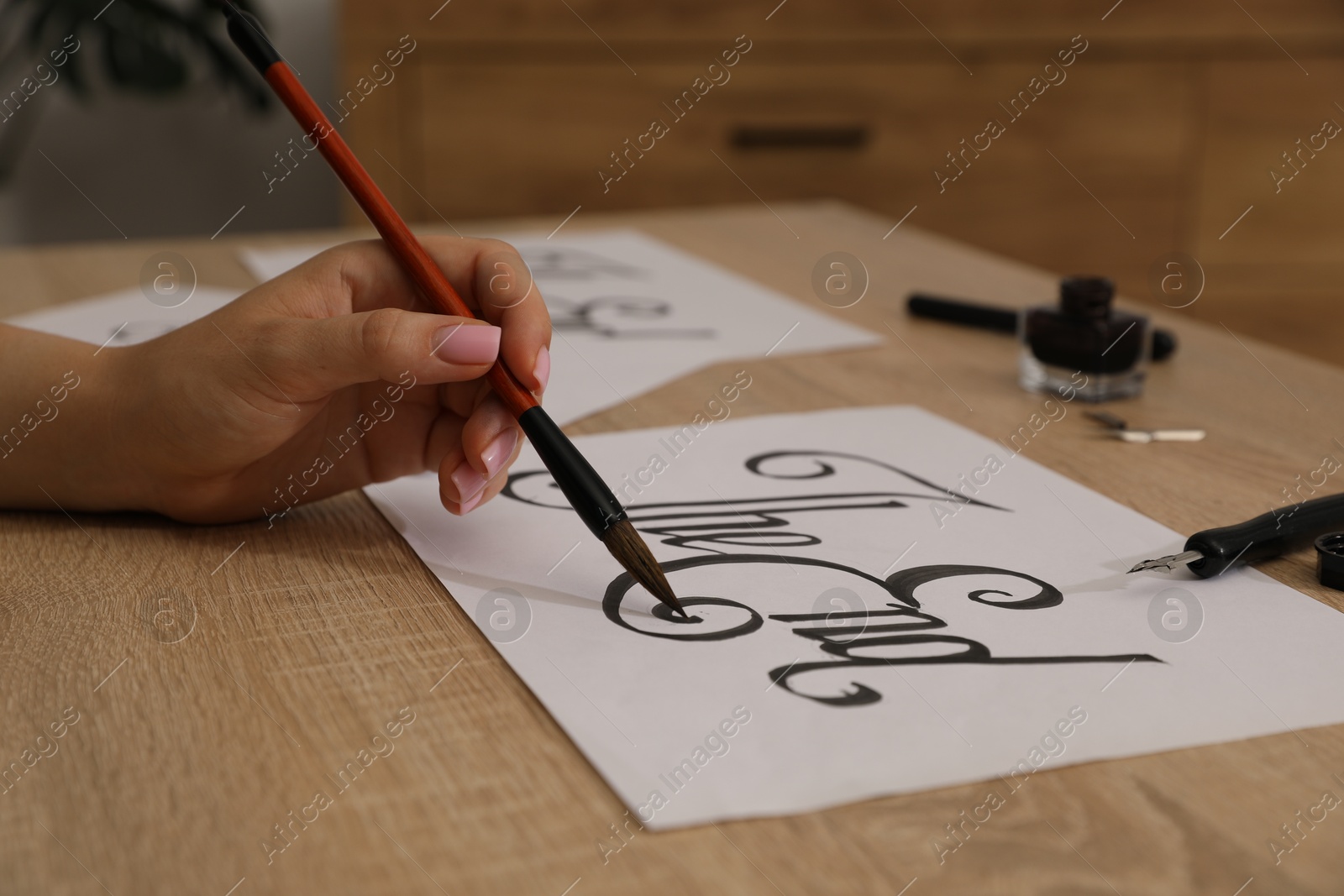 Photo of Calligraphy. Woman with brush writing words The End on sheet of paper at wooden table, closeup