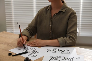 Photo of Calligraphy. Woman with brush writing words The End on sheet of paper at wooden table, closeup