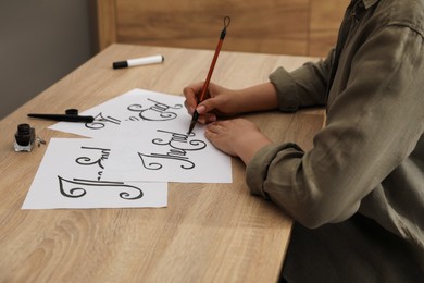 Photo of Calligraphy. Woman with brush writing words The End on sheet of paper at wooden table, closeup