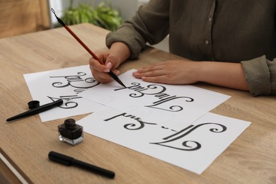 Photo of Calligraphy. Woman with brush writing words The End on sheet of paper at wooden table, closeup