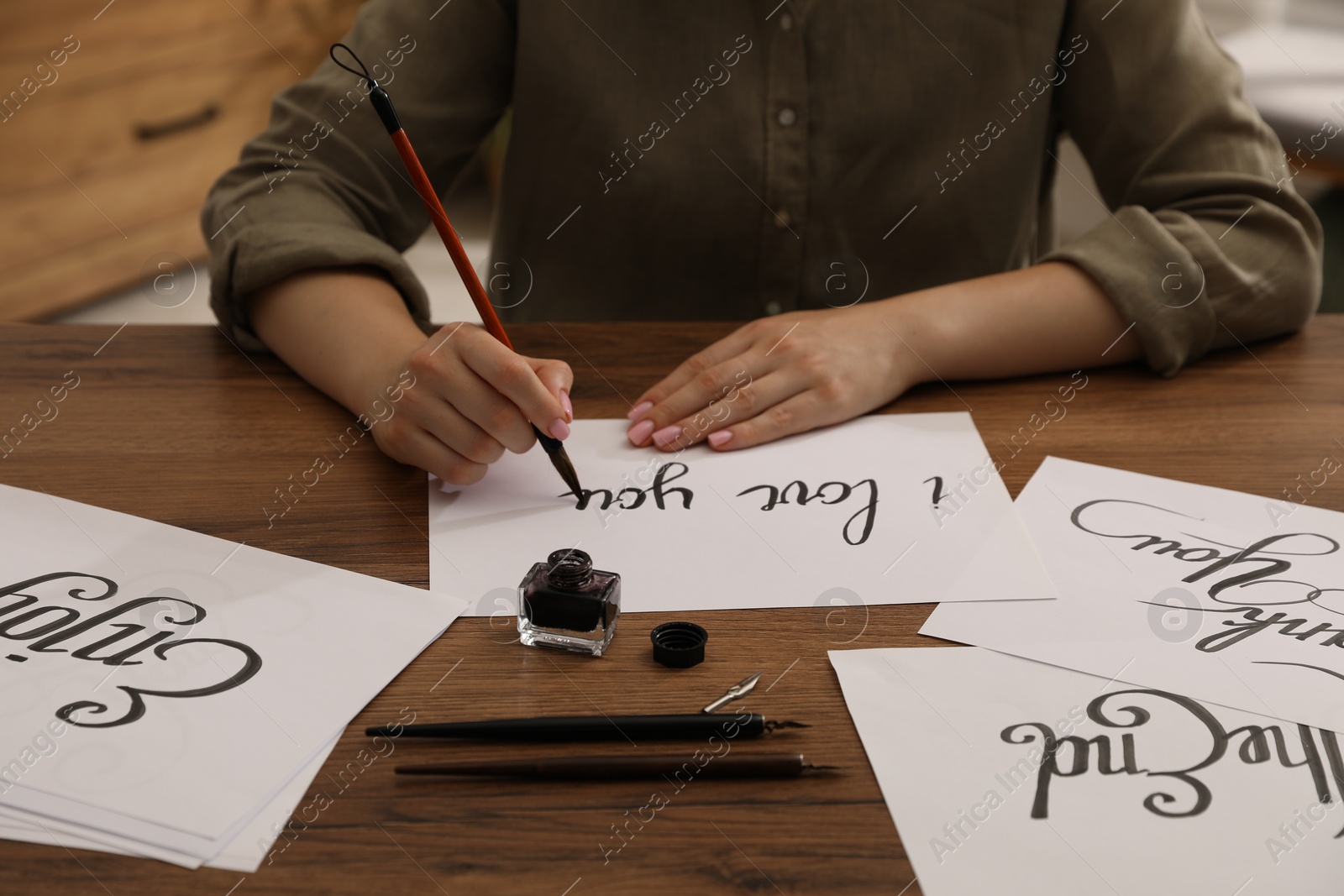 Calligraphy. Woman with brush writing phrase I Love You on sheet of paper at wooden table, closeup Photo of Calligraphy. Woman with brush writing phrase I Love You on sheet of paper at wooden table, closeup