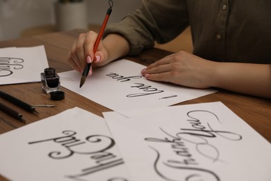 Photo of Calligraphy. Woman with brush writing phrase I Love You on sheet of paper at wooden table, closeup