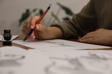 Photo of Calligraphy. Woman with brush, ink and handwritten cards at table, closeup