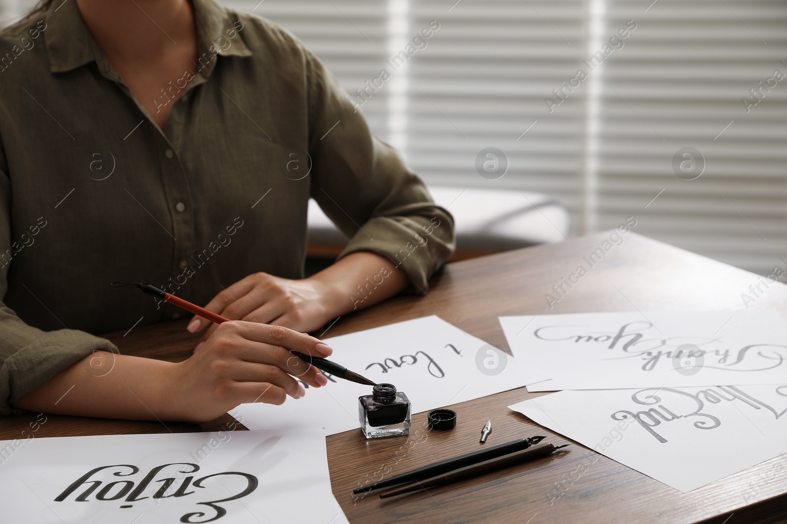 Woman with calligraphy tools and handwritten cards at wooden table indoors, closeup Photo of Woman with calligraphy tools and handwritten cards at wooden table indoors, closeup