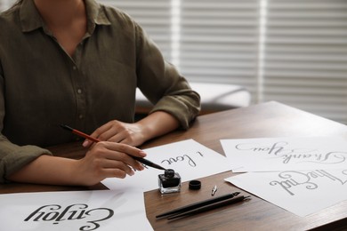 Photo of Woman with calligraphy tools and handwritten cards at wooden table indoors, closeup