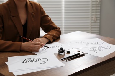 Photo of Woman with calligraphy tools and handwritten cards at wooden table indoors, closeup