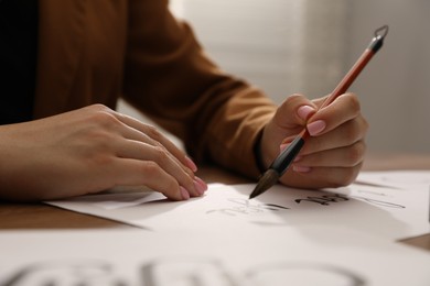 Photo of Calligraphy. Woman with brush writing phrase I Love You on sheet of paper at table, closeup