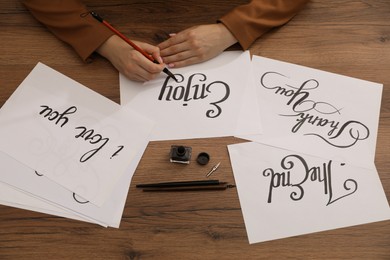 Photo of Calligraphy. Woman with brush writing word Enjoy on sheet of paper at wooden table, top view
