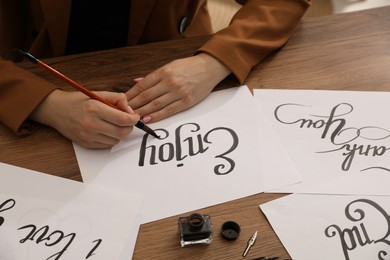 Photo of Calligraphy. Woman with brush writing word Enjoy on sheet of paper at wooden table, closeup