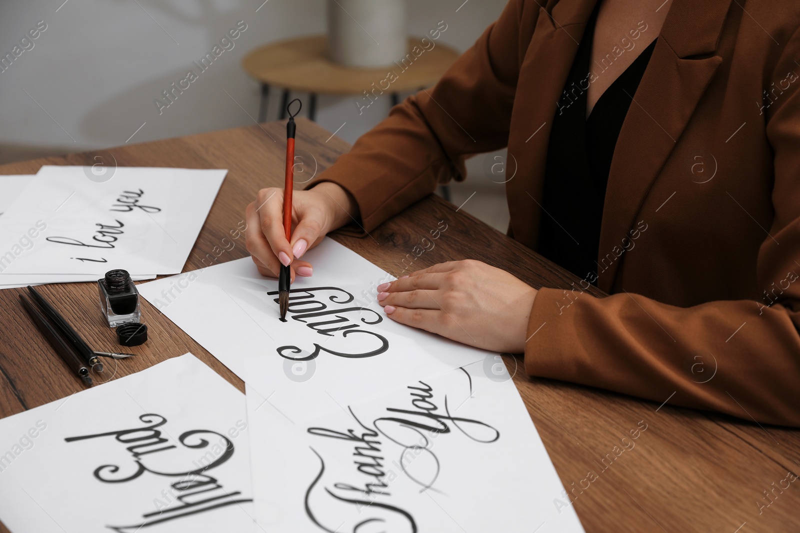 Calligraphy. Woman with brush writing word Enjoy on sheet of paper at wooden table, closeup Photo of Calligraphy. Woman with brush writing word Enjoy on sheet of paper at wooden table, closeup