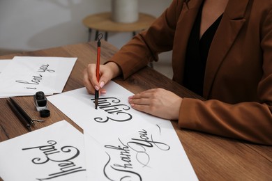 Photo of Calligraphy. Woman with brush writing word Enjoy on sheet of paper at wooden table, closeup