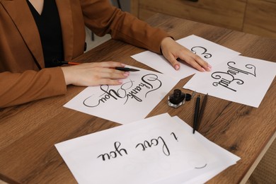 Photo of Woman with calligraphy tools and handwritten cards at wooden table indoors, closeup