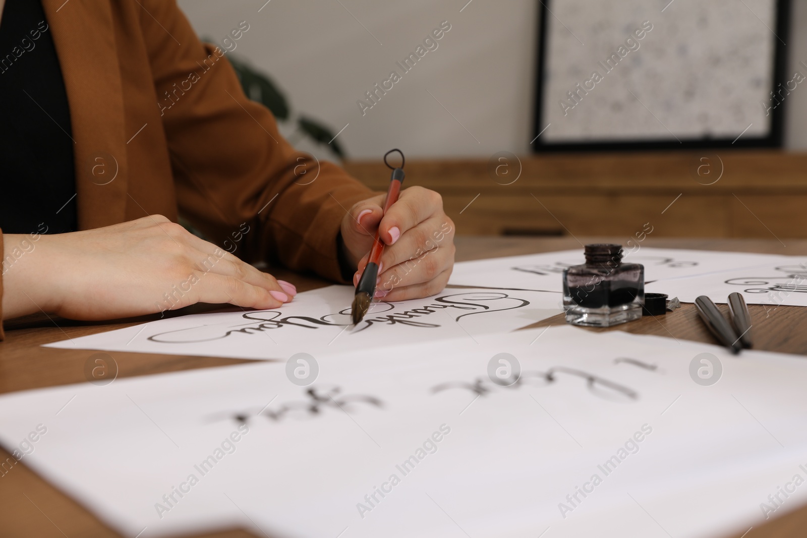 Calligraphy. Woman with brush writing words Thank You on sheet of paper at wooden table, closeup Photo of Calligraphy. Woman with brush writing words Thank You on sheet of paper at wooden table, closeup