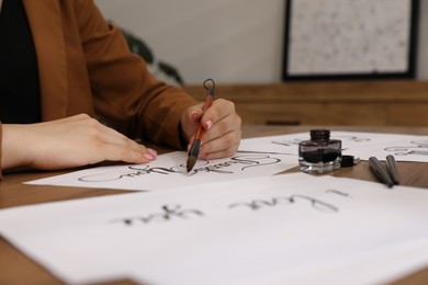 Photo of Calligraphy. Woman with brush writing words Thank You on sheet of paper at wooden table, closeup