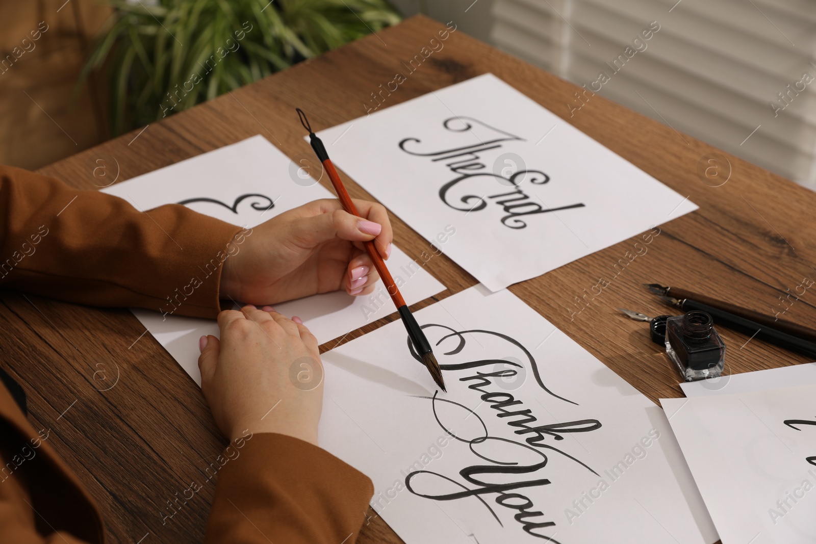 Calligraphy. Woman with brush writing words Thank You on sheet of paper at wooden table, closeup Photo of Calligraphy. Woman with brush writing words Thank You on sheet of paper at wooden table, closeup