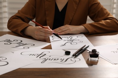 Photo of Calligraphy. Woman with brush writing phrase I Love You on sheet of paper at wooden table, closeup