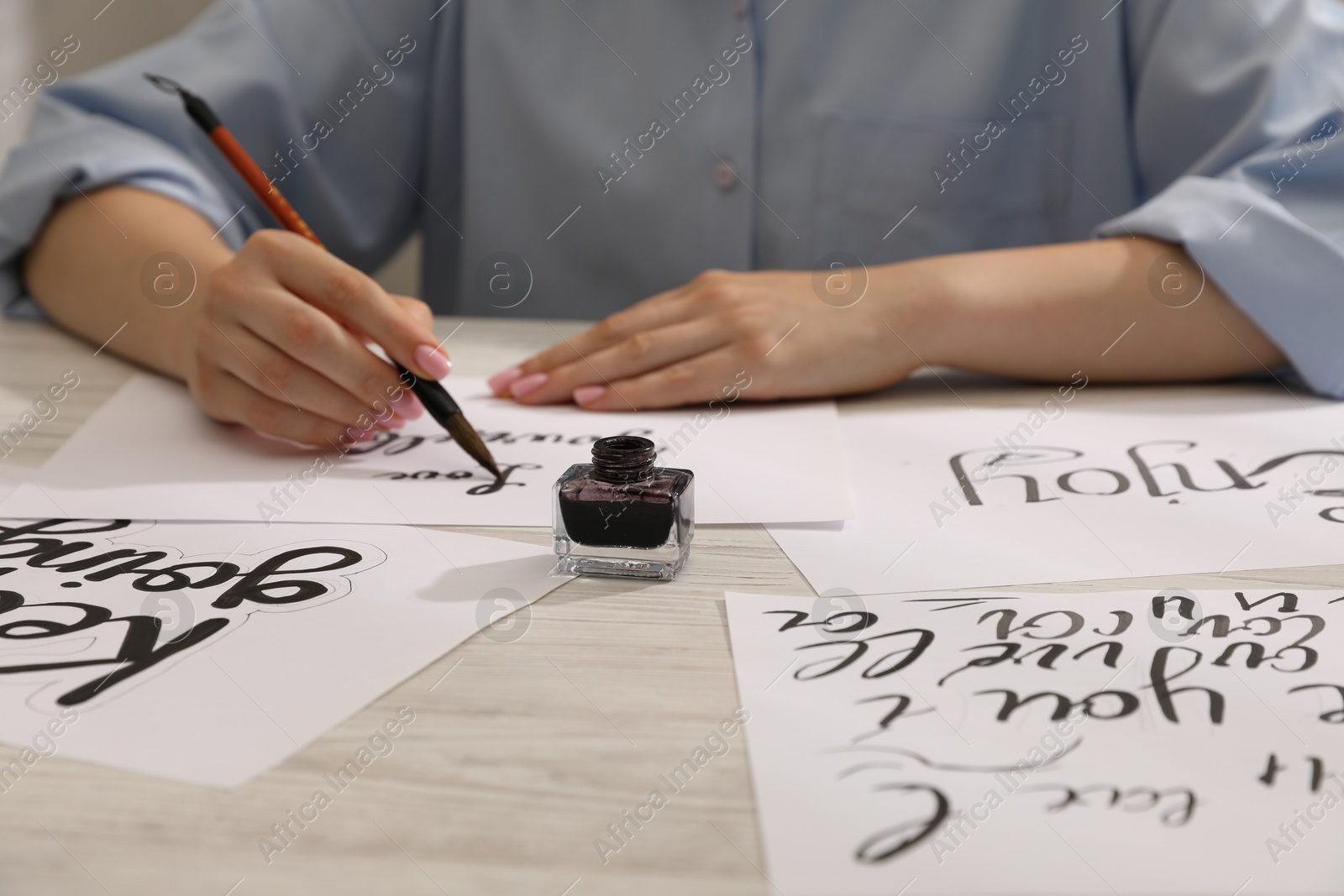 Calligraphy. Woman with brush writing on sheet of paper at wooden table, closeup Photo of Calligraphy. Woman with brush writing on sheet of paper at wooden table, closeup