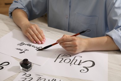 Photo of Calligraphy. Woman with brush writing phrase Love Yourself on sheet of paper at wooden table, closeup