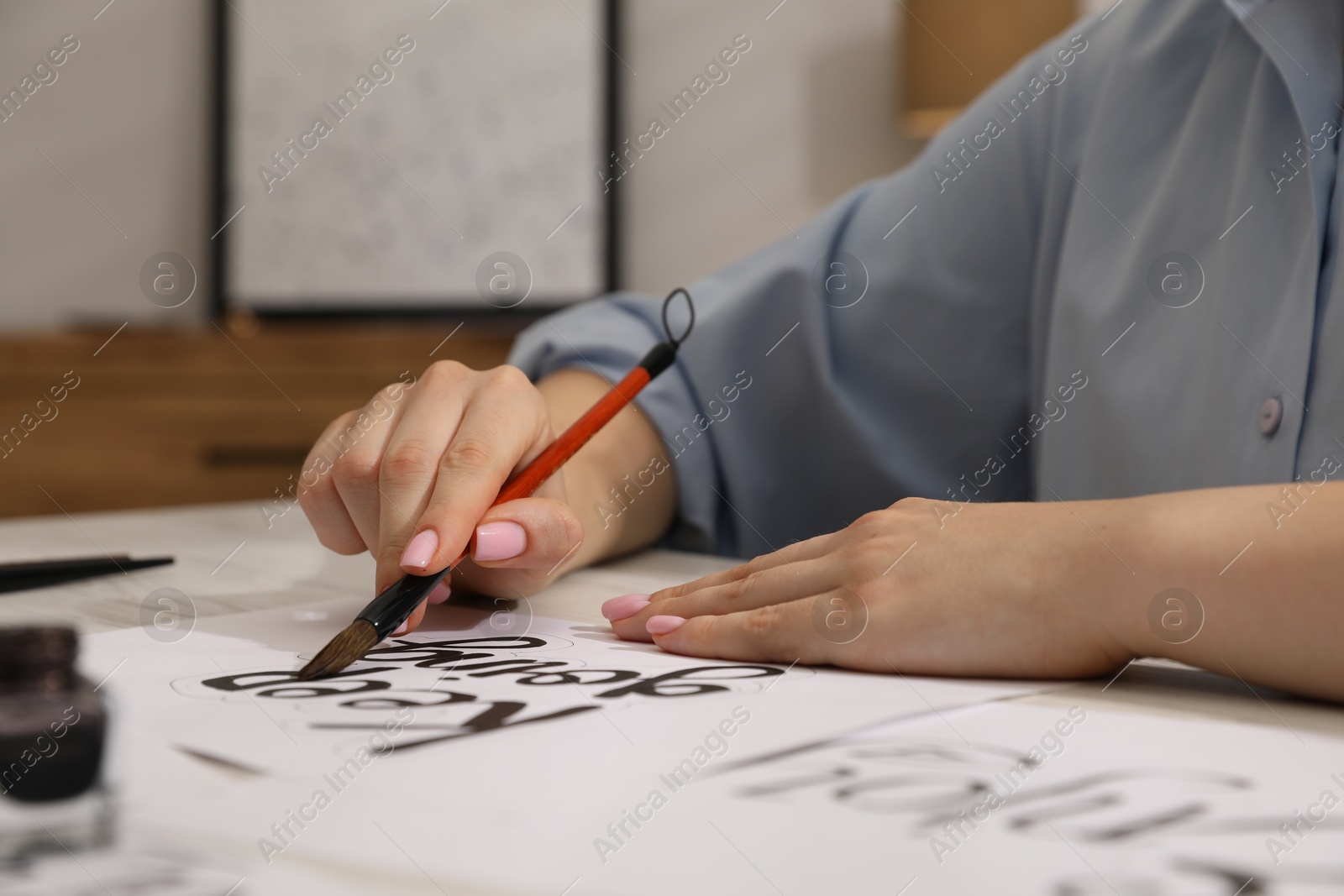 Calligraphy. Woman with brush writing phrase Keep Going on sheet of paper at table indoors, closeup Photo of Calligraphy. Woman with brush writing phrase Keep Going on sheet of paper at table indoors, closeup