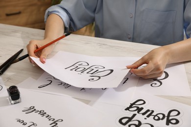 Photo of Woman with calligraphy tools and handwritten cards at wooden table indoors, closeup