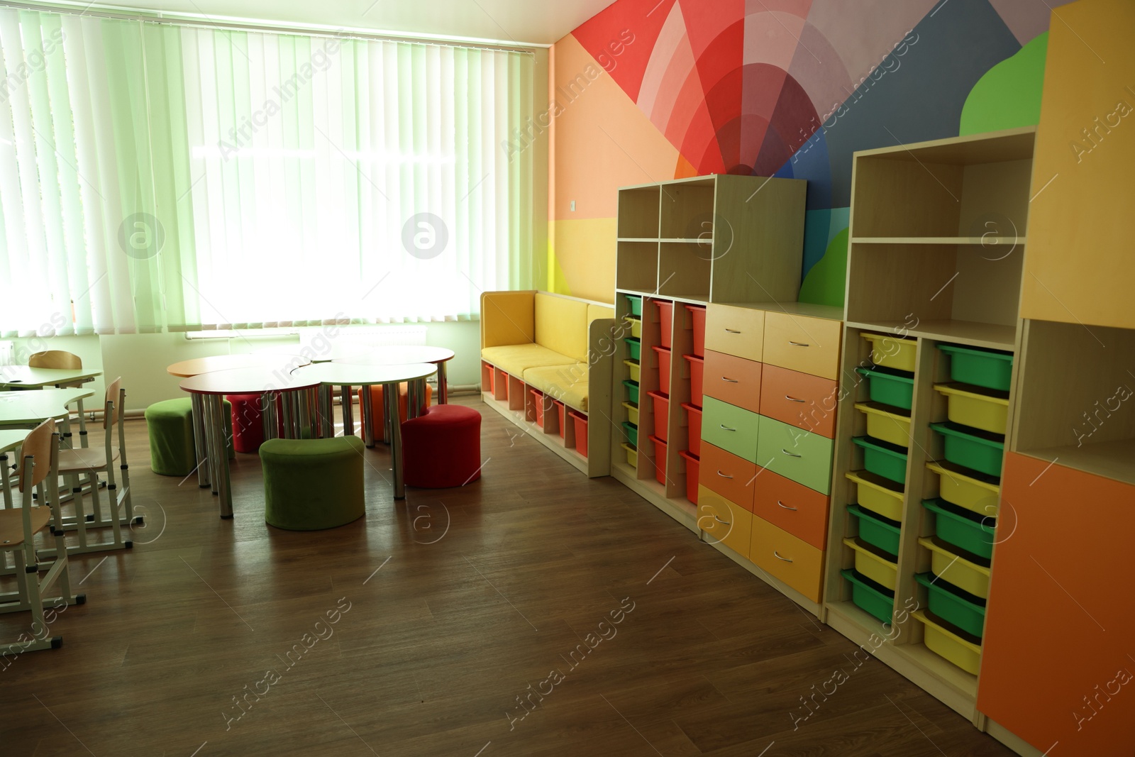 Photo of Desks, chairs and shelving unit near bright wall in classroom
