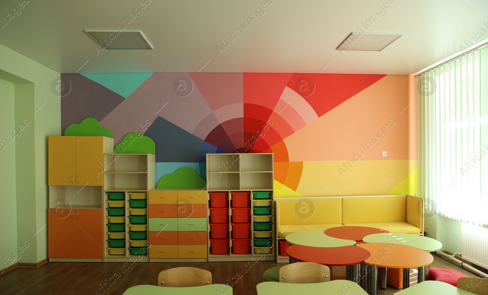 Photo of Desks, chairs and shelving unit near bright wall in classroom