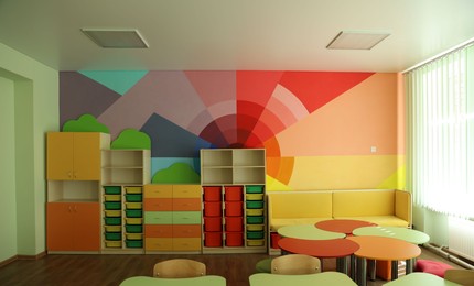 Photo of Desks, chairs and shelving unit near bright wall in classroom