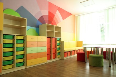 Photo of Desks, chairs and shelving unit near bright wall in classroom