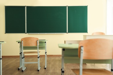 Photo of Desks with chairs and green chalkboard in classroom, selective focus