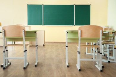 Photo of Desks with chairs and green chalkboard in classroom, selective focus