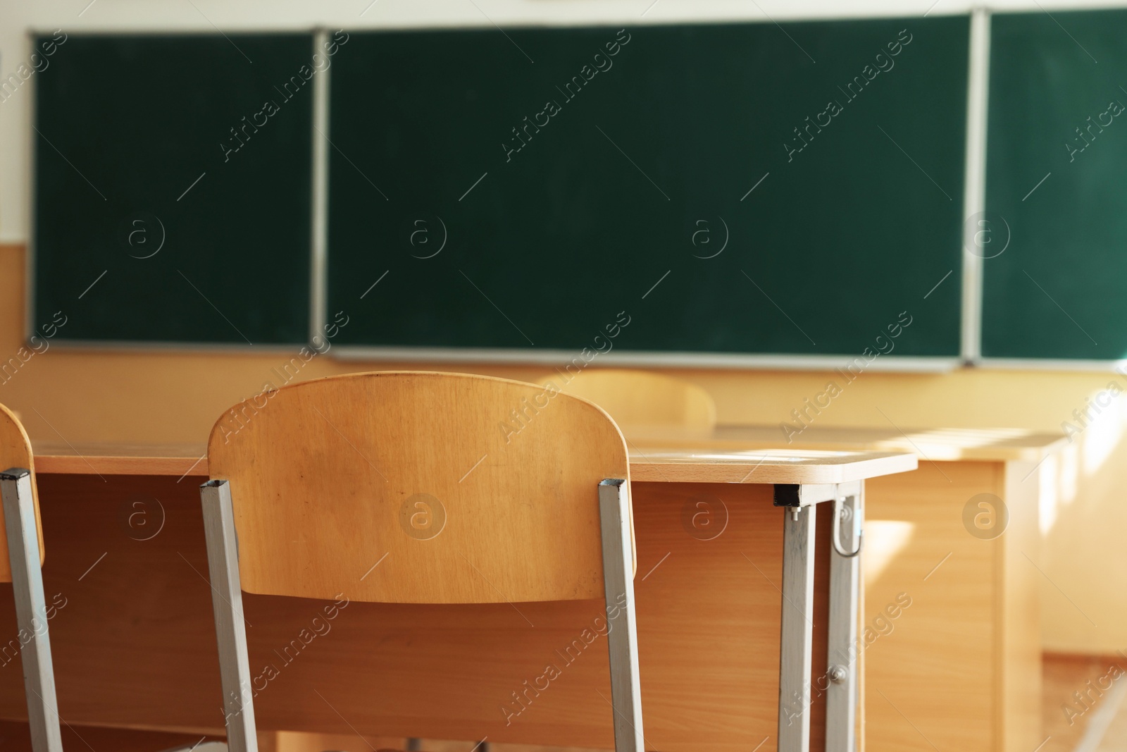 Photo of Desks with chairs and green chalkboard in classroom, selective focus