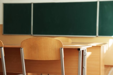 Photo of Desks with chairs and green chalkboard in classroom, selective focus