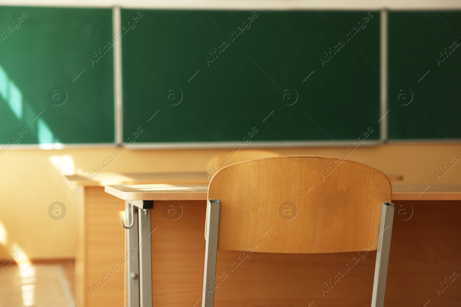 Photo of Desks with chairs and green chalkboard in classroom, selective focus